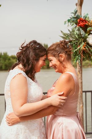 Emotional moment shared between two people under floral wedding arch by the water.