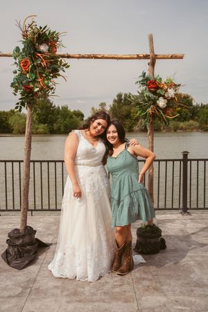 Wedding party poses beneath floral arch on waterfront deck with lake views.