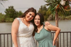 Two women pose together against a waterfront railing at an outdoor event in warm evening light.