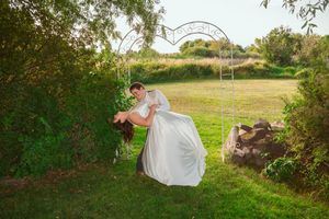 A romantic garden scene with a white flowy wedding dress dips under a decorative metal arbor on green grass.