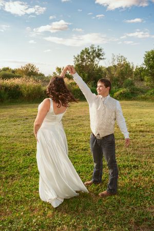 A couple dancing together in a sunlit field with trees in the background.