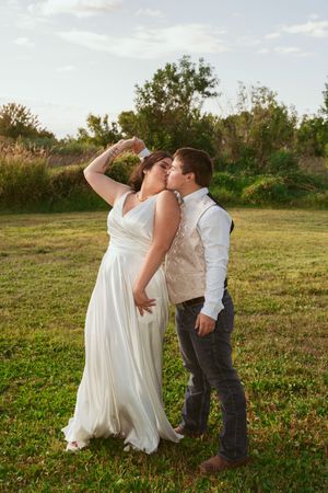 Playful wedding couple dances on grassy field during outdoor celebration.