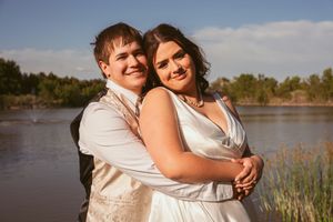 Happy couple shares intimate moments and laughter by a lakeside during a sunset photoshoot.