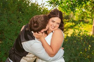 A joyful couple embracing outdoors with lush greenery and golden sunlight in the background.