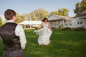 A couple shares a playful moment on a lawn with a white tent in the background.
