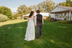 Newlyweds stroll together on expansive lawn with white houses visible in distance.