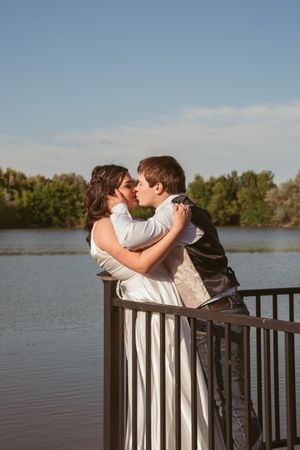 A couple embraces on a deck overlooking a serene lake at sunset.