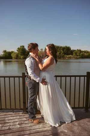Couple shares romantic moment on waterfront deck during sunset wedding celebration.