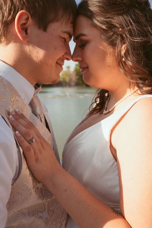 An intimate close-up moment between newlyweds in formal wedding attire against a lakeside background.