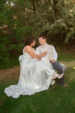 A couple in wedding attire lounges together on lush green grass during a romantic outdoor photoshoot.