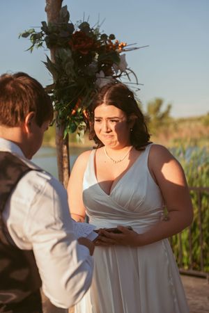 Couple embraces during golden hour wedding photoshoot near a lake with floral decorations.