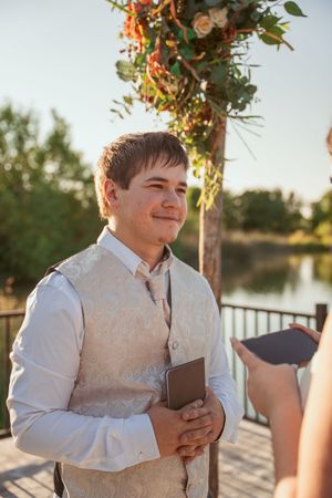 A collage of three images showing someone in a cream vest and white shirt smiling during a waterfront wedding ceremony.