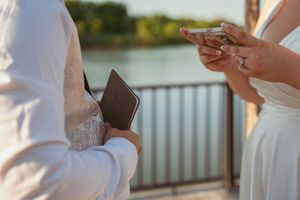 Close-up of hands exchanging wedding rings during an outdoor waterfront ceremony.