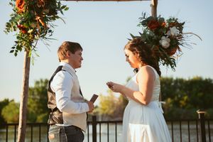 A romantic outdoor wedding ceremony at sunset with floral archway decorations and waterfront backdrop.