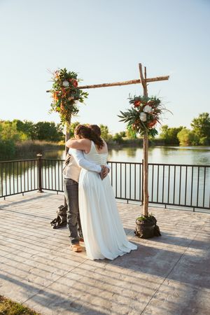 Newlyweds share intimate moments on lakeside deck during sunset ceremony.