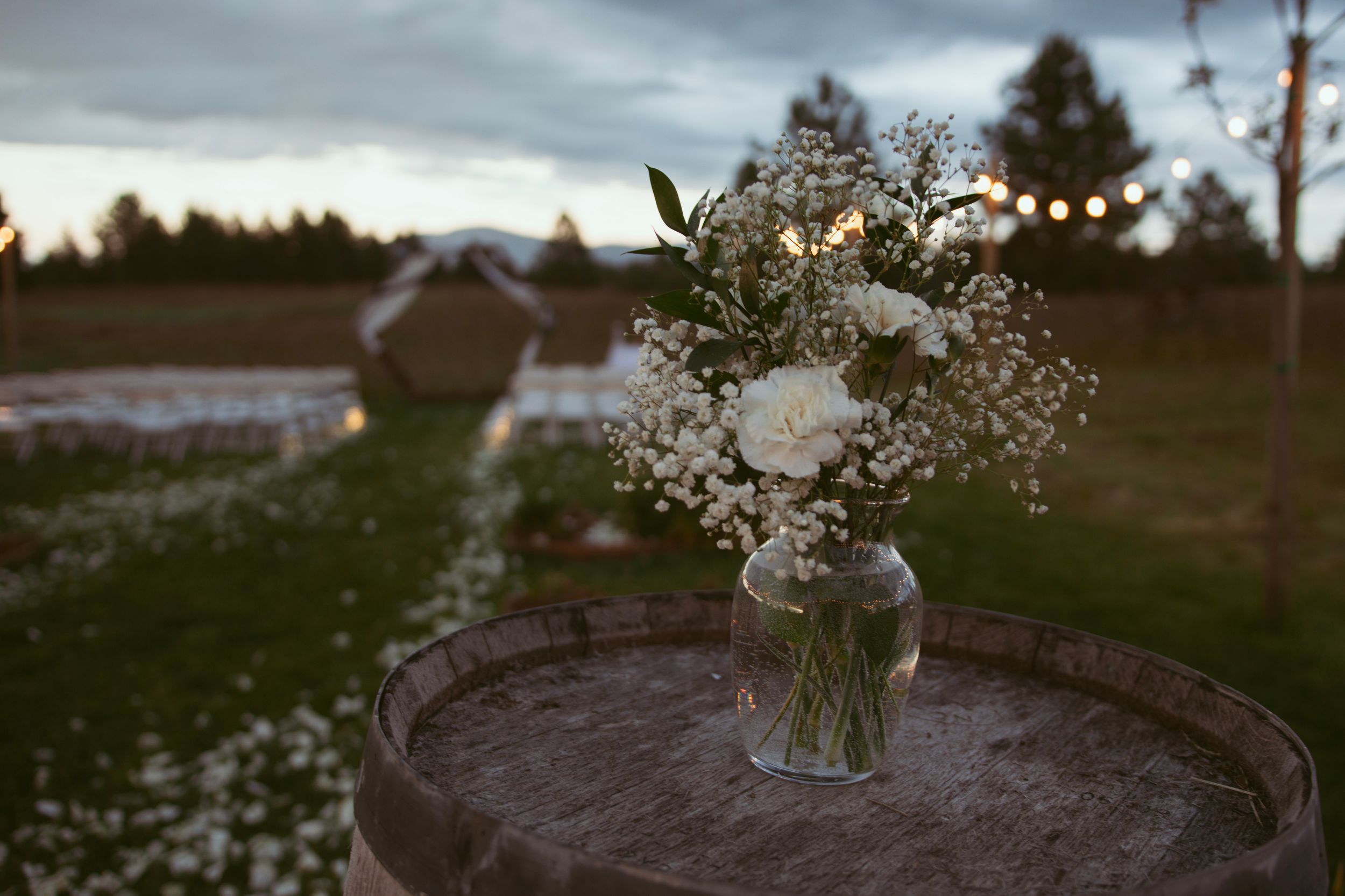 A rustic garden setting at sunset with fresh white floral centerpieces arranged in antique stone vessels.