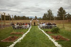White flower petals line the aisle of an outdoor wedding ceremony setup with guests seated under cloudy skies.