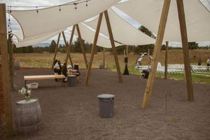 String lights illuminate an outdoor event space with wooden posts and sandy ground during sunset.