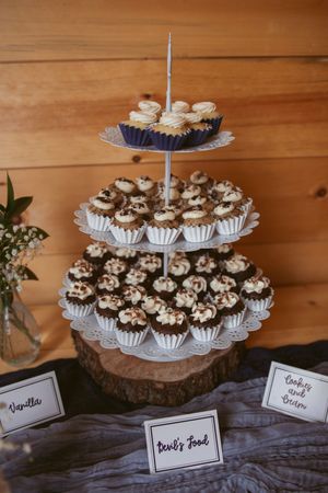 Three-tiered dessert stand displaying chocolate cupcakes on a wooden surface with name cards.