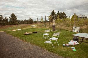 Rustic outdoor wedding venue setup with white chairs and wooden benches on grassy area.