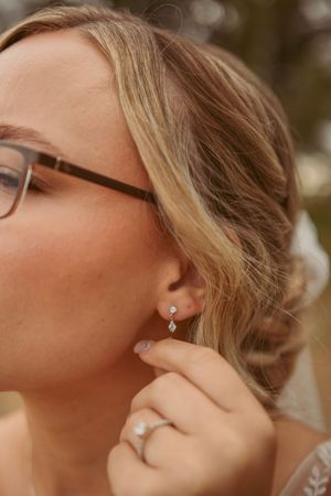 A close-up shot of blonde hair, glasses, and a delicate earring being touched with a manicured hand.