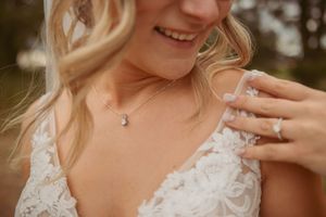 Close up of lace wedding dress detail and jewelry on a sunny day.