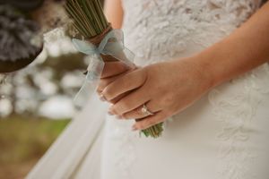 Close-up of hands holding a wedding bouquet, showcasing a beautiful engagement ring.