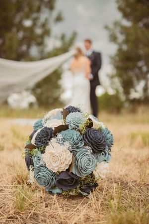 A wedding bouquet with blue and cream succulents in the foreground with a blurred couple in the background.