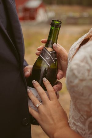 Couple holding green glass bottles showing their wedding rings during celebration.