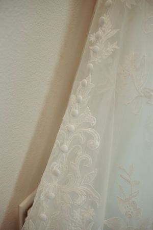 Intricate lace embroidery detail of white wedding dress against neutral wall.