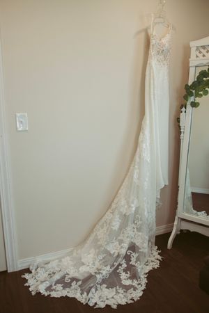 White lace wedding dress displayed in a bridal boutique fitting room with a long floral train and delicate details.