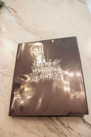 Black wedding album cover with metallic floral design on marble surface.