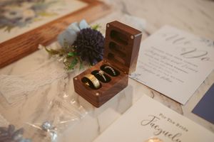 Rustic wooden ring box with gold wedding bands displayed on lace tablecloth with floral decor.
