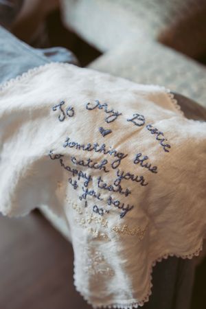 A white handkerchief embroidered with blue text and delicate lace trim on the edges.