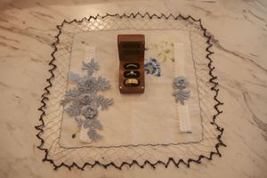 A white embroidered handkerchief with blue floral patterns and a dark brown wooden box on marble surface.