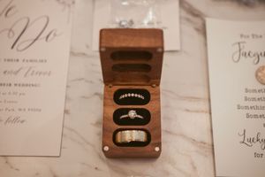 Wedding rings displayed in a wooden ring box on display with invitation paper in the background.