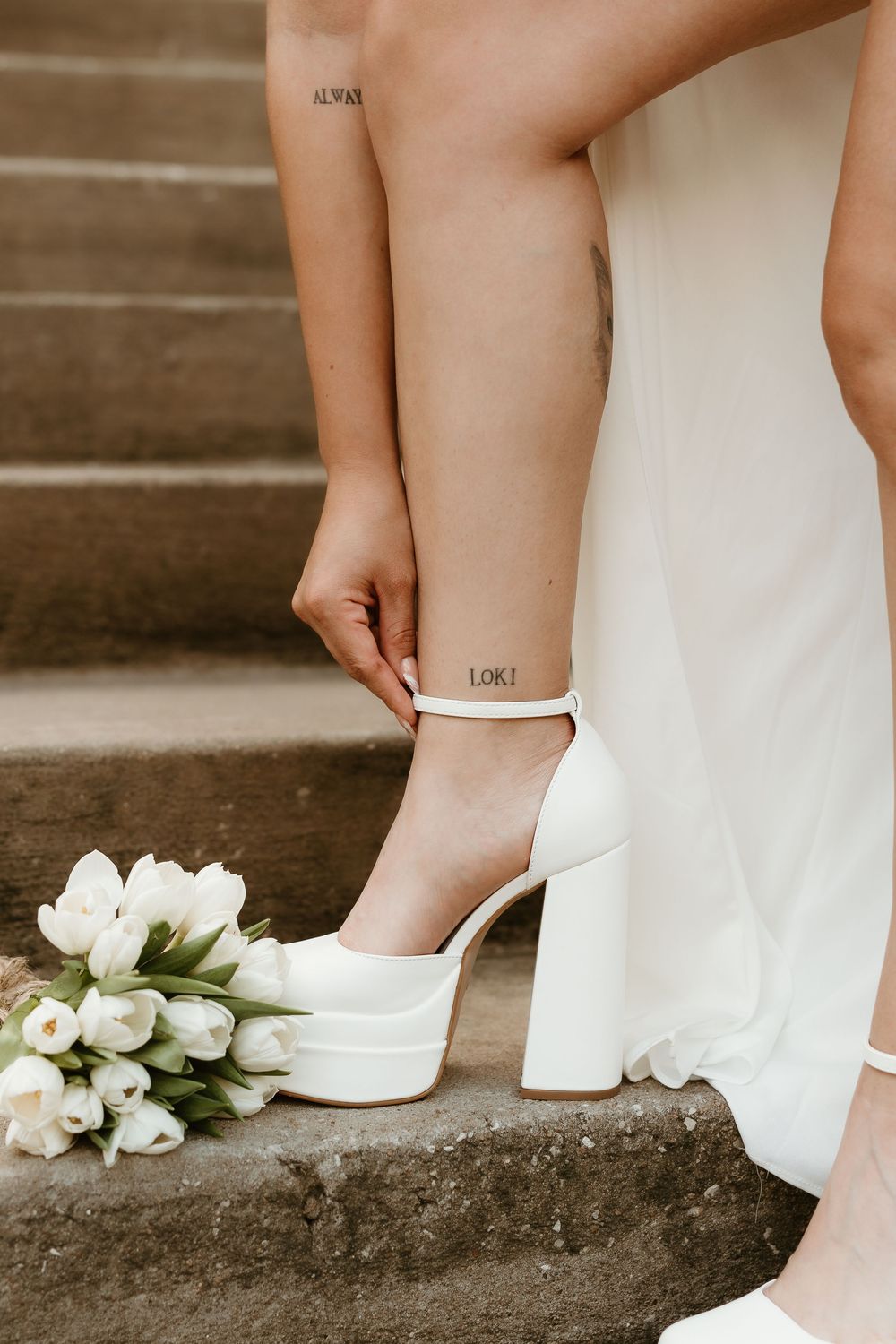 White platform wedding shoes and bouquet of white tulips on stone steps.