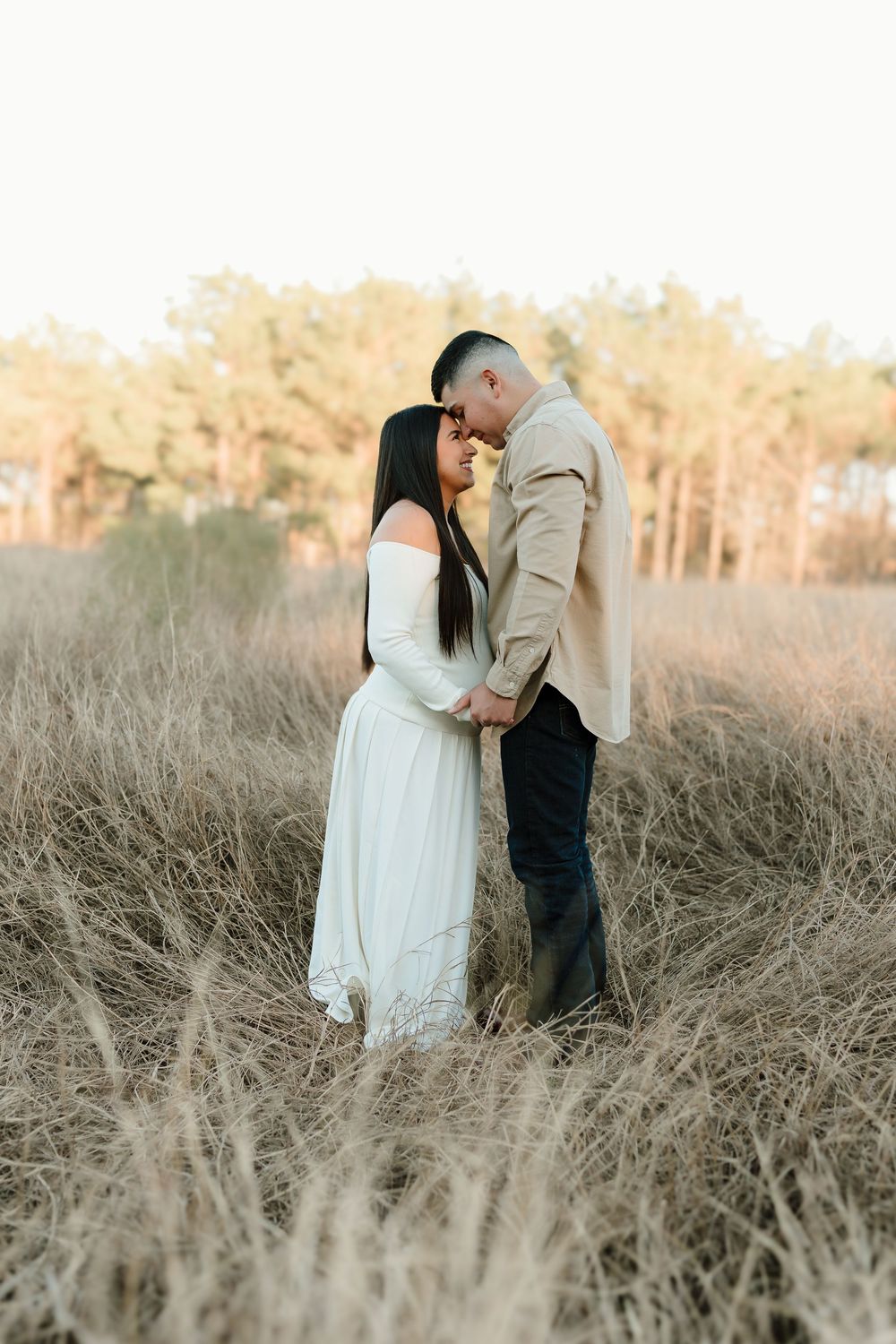 Couple embracing in tall grass field during golden hour.