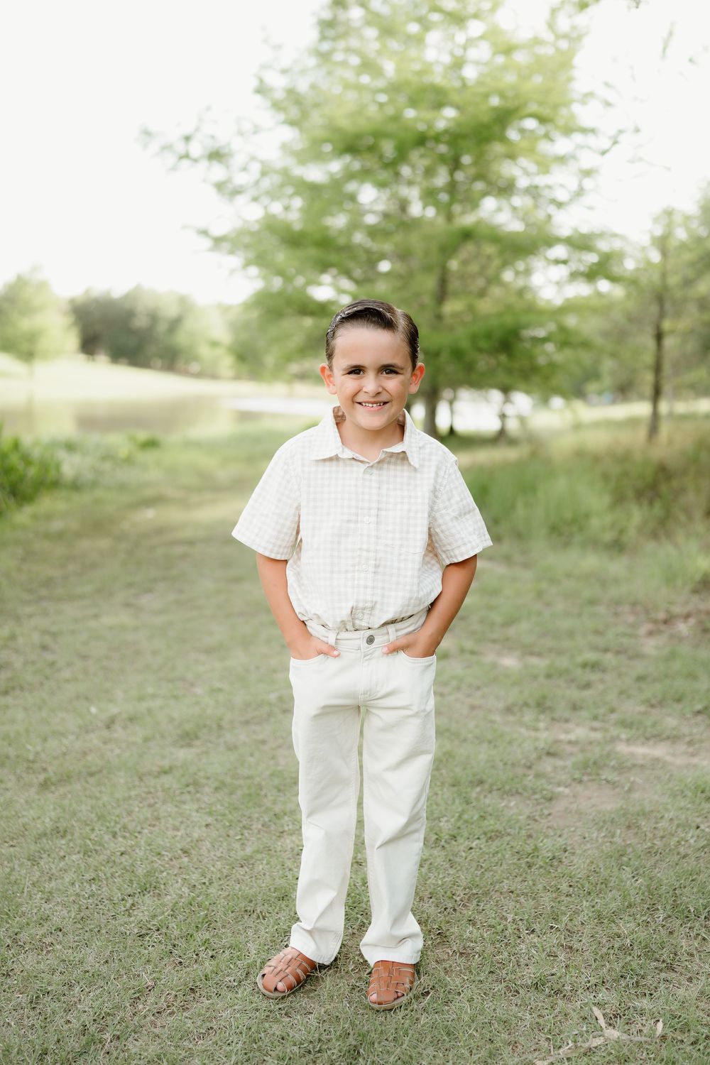 Child in all-white outfit standing outdoors on grassy field.