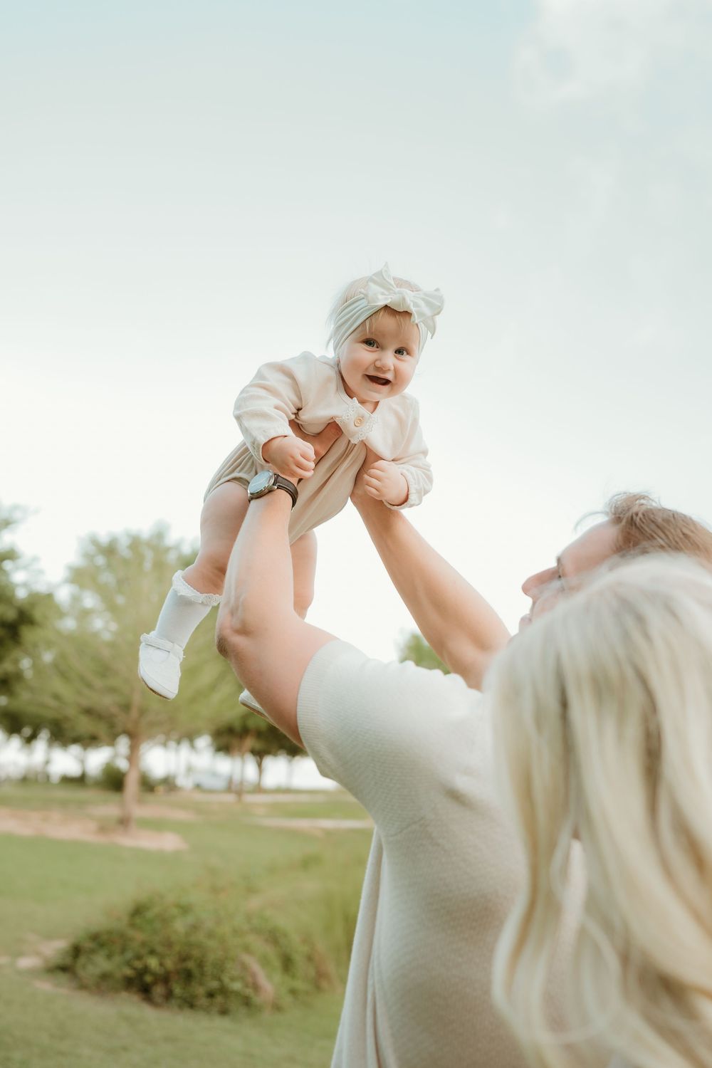 Series of joyful moments lifting and playing with a baby outdoors in white clothing.