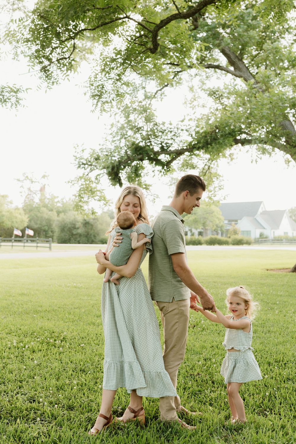 Family in coordinating green outfits plays together in sunny park setting.