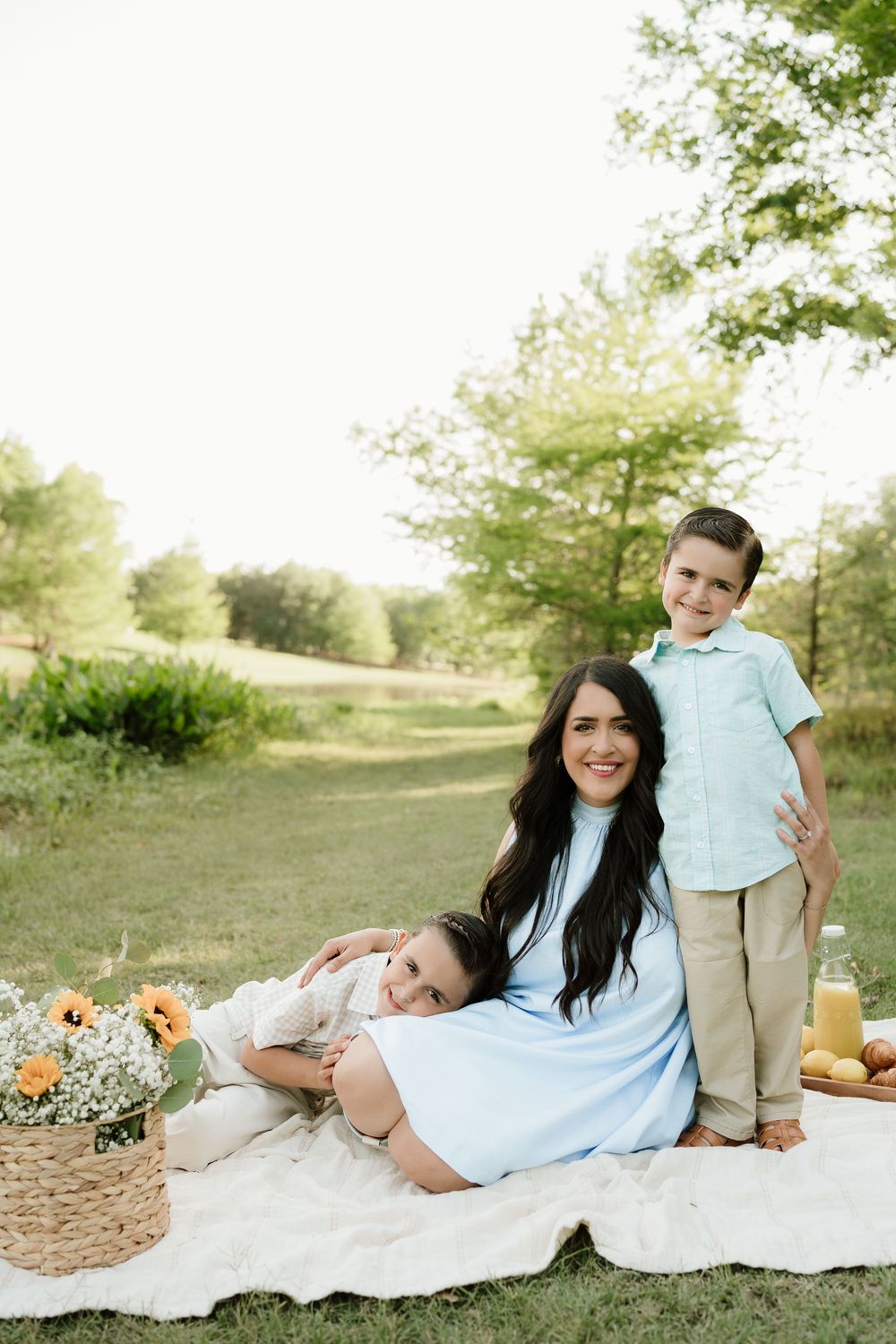 Family having picnic on white blanket with flowers and refreshments in outdoor setting.