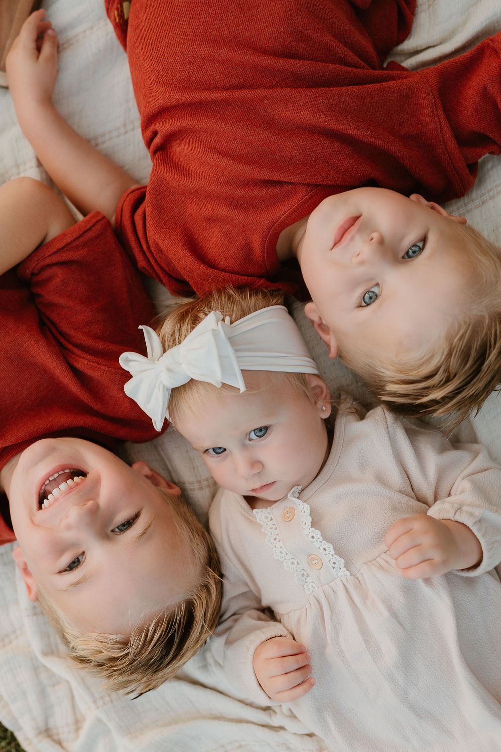 Baby in red sweater lying on white bedding with bright blue eyes and sweet expressions.