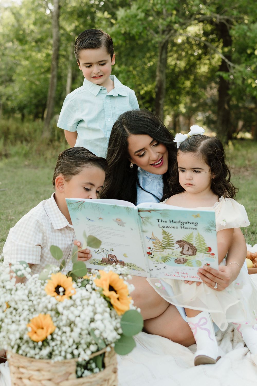Family reading storybook together on picnic blanket with flowers outdoors.