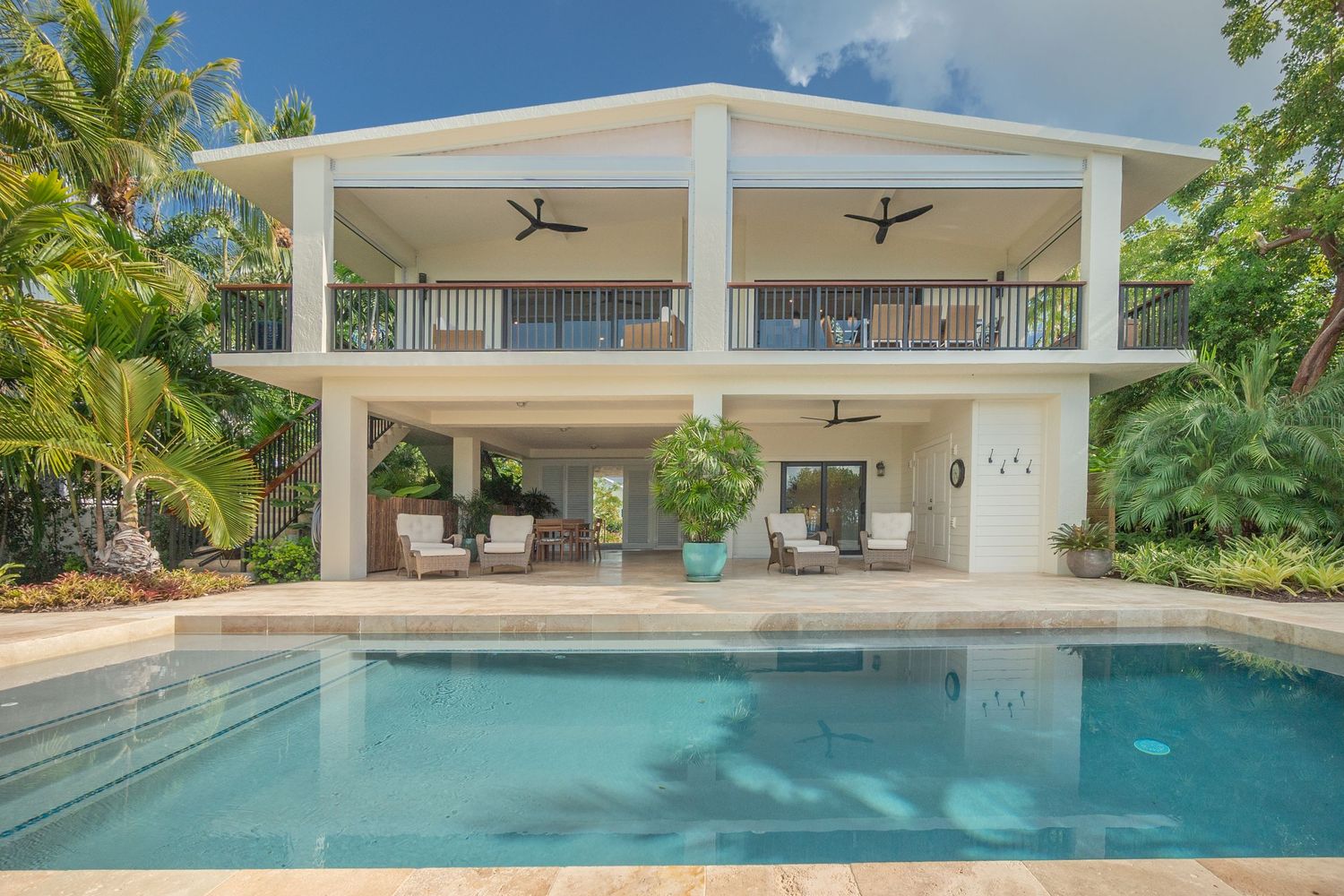 Modern two-story white beach house with covered patio and swimming pool.