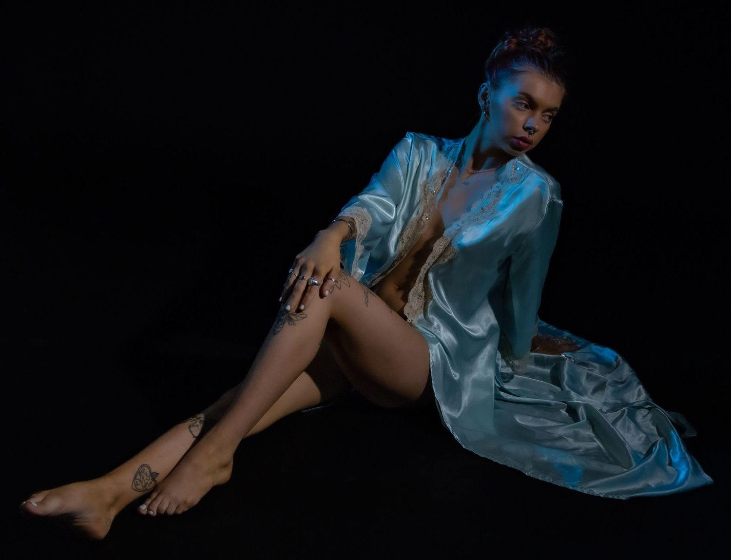 A figure in a flowing blue silk robe poses dramatically against a dark background with artistic lighting.