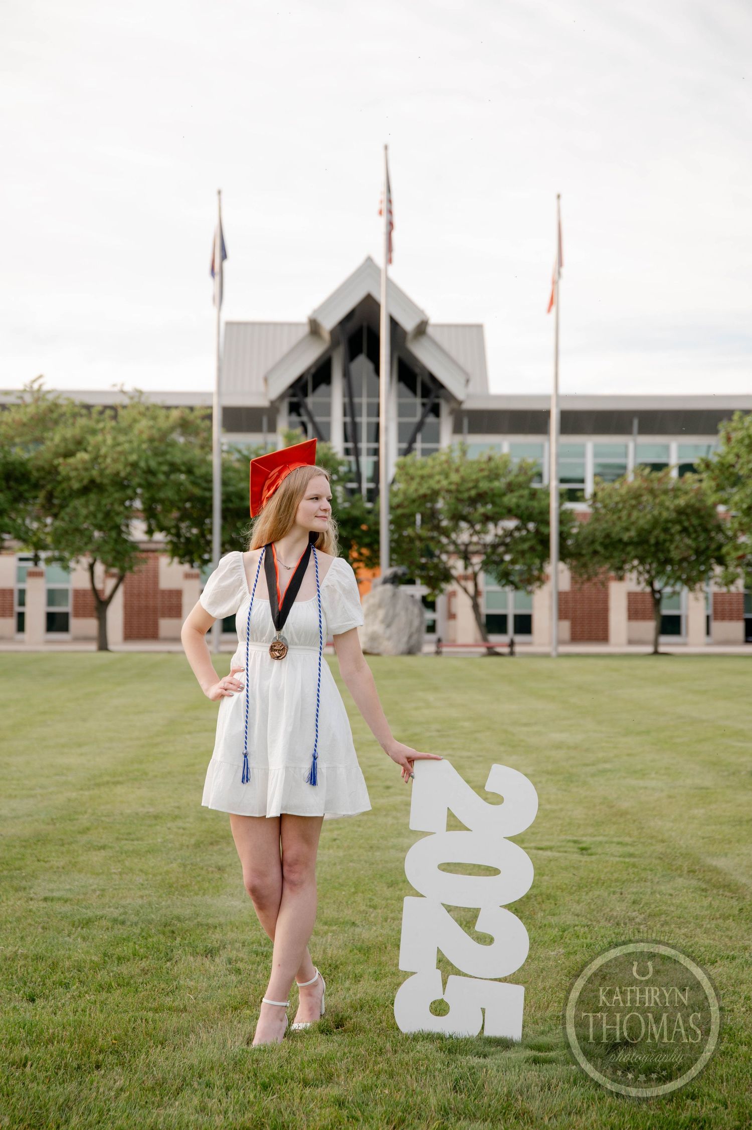 Graduation photos set on college campus lawn with large decorative "2022" numerals and modern building in background.