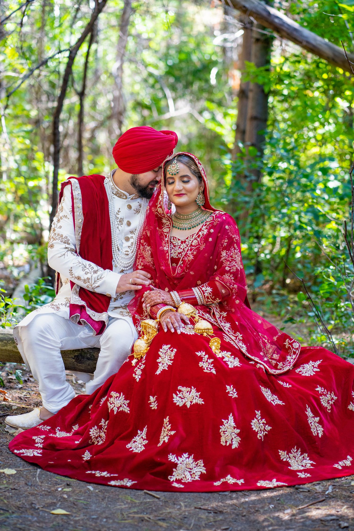 A couple in traditional Indian wedding attire poses in a forest setting.