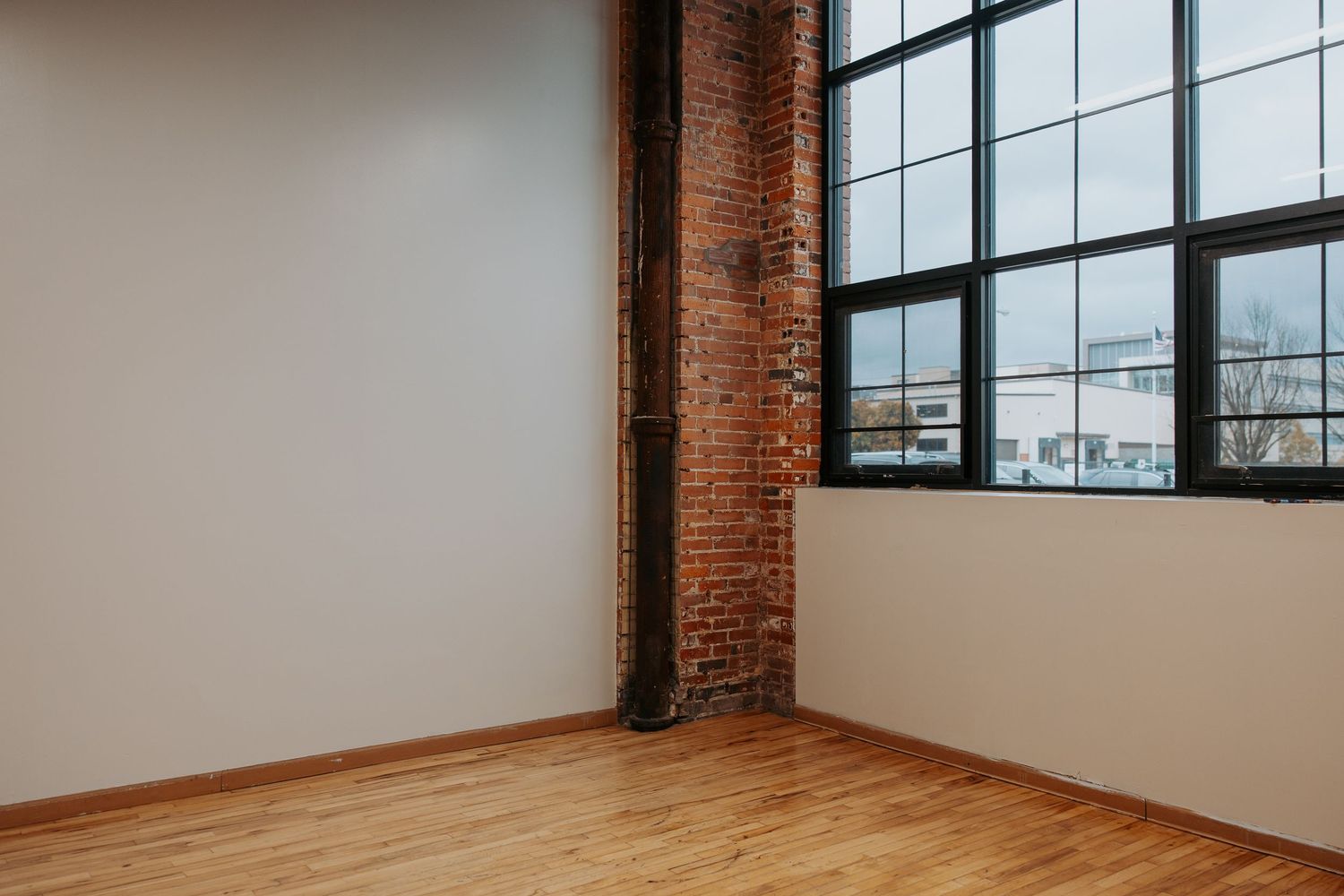A minimalist studio interior with a director's chair, potted plant, and sheer white curtains on wooden flooring.