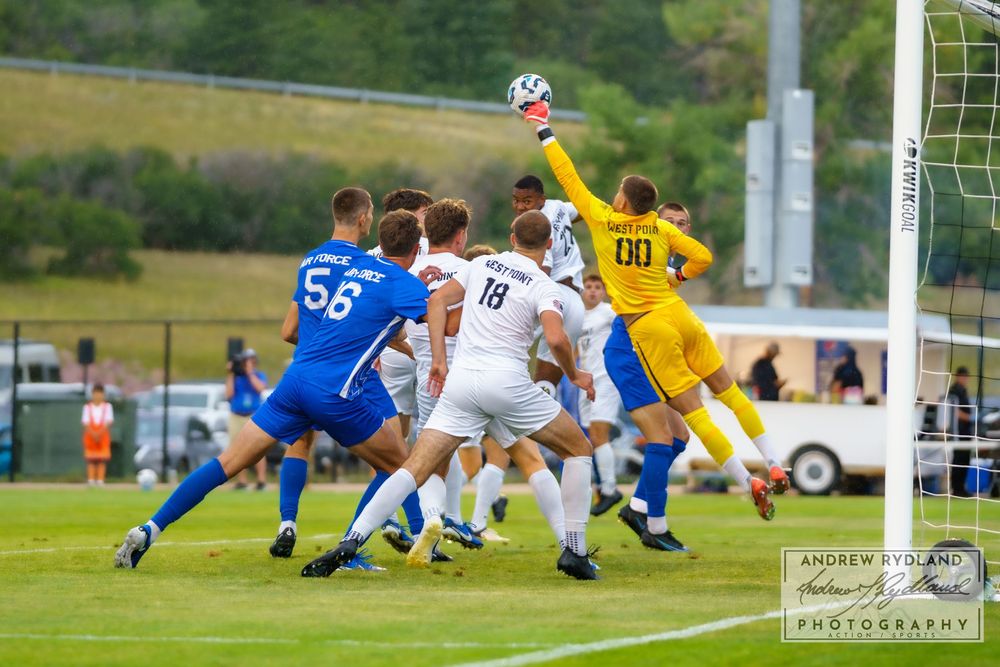 Soccer players compete for a header in front of the goal during an intense match.